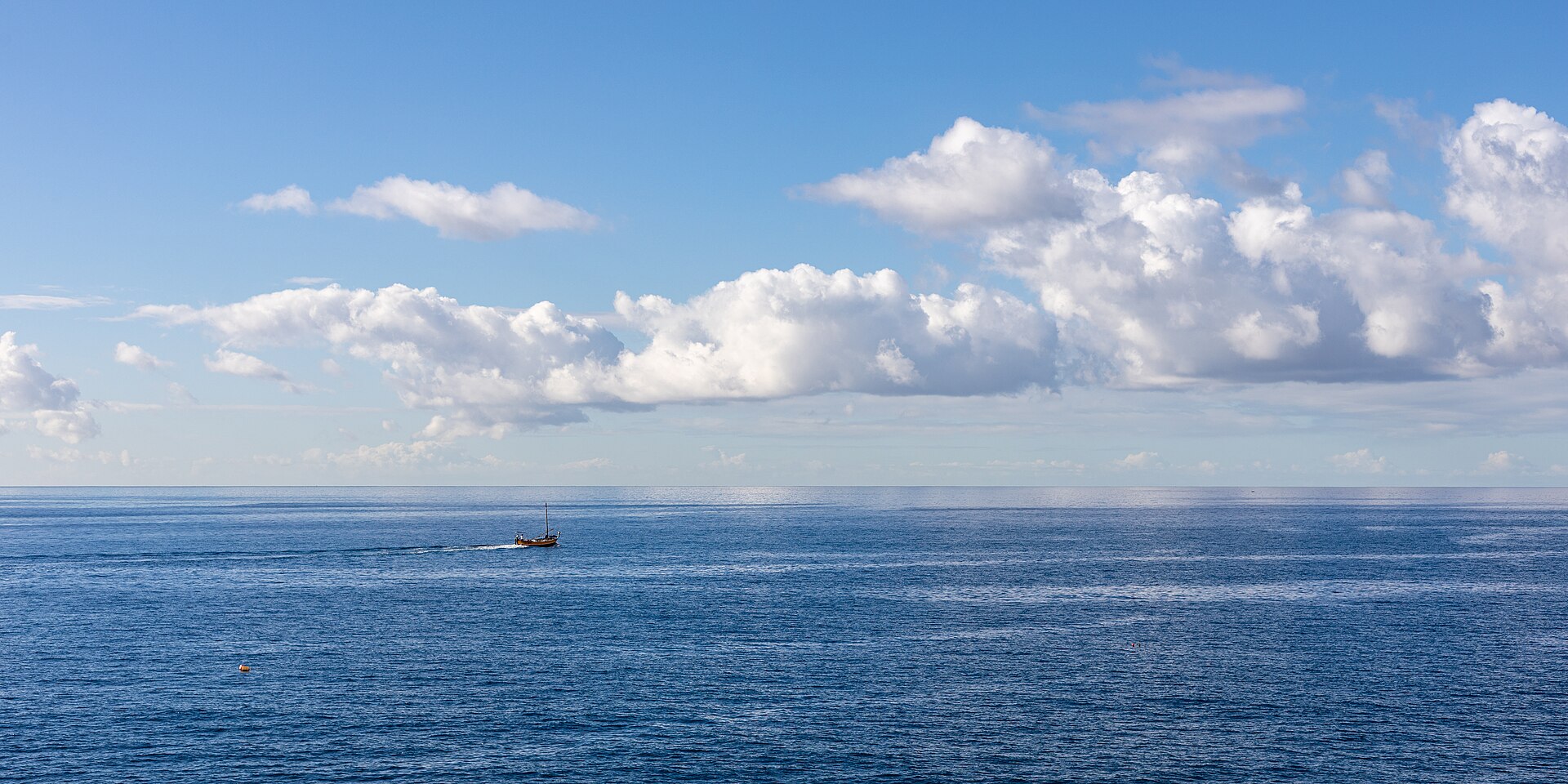 A lone boat far out on a vast, flat sea, seen from a hilltop lookout on shore