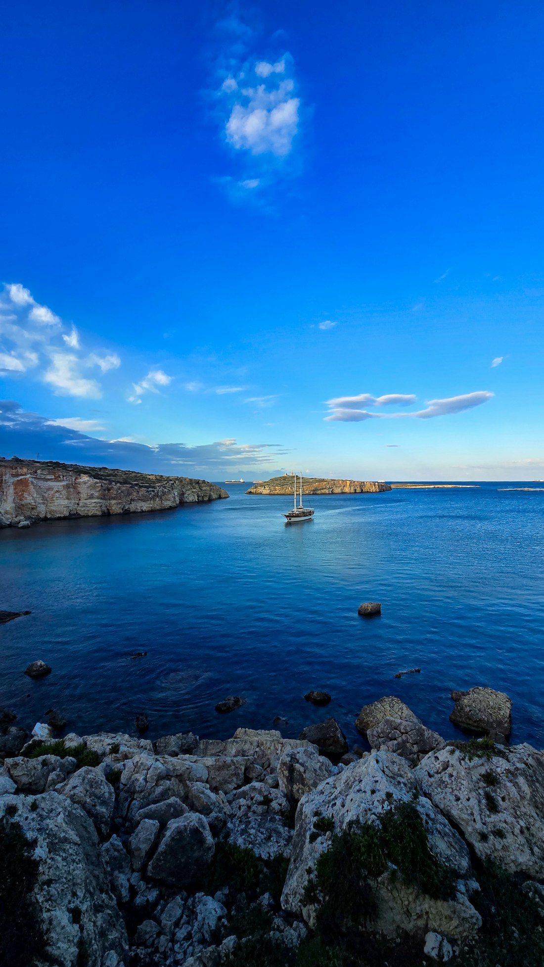 A sailboat anchored in a turquoise cove between rocky cliffs