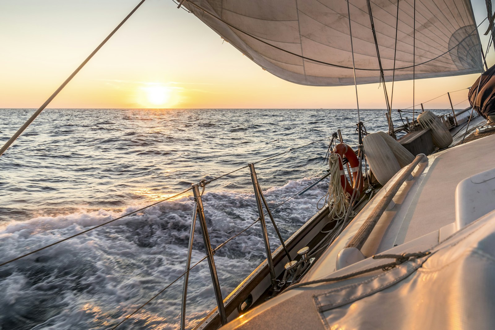 Sailing from the deck of a boat at golden hour, sails overhead and the wake trailing behind