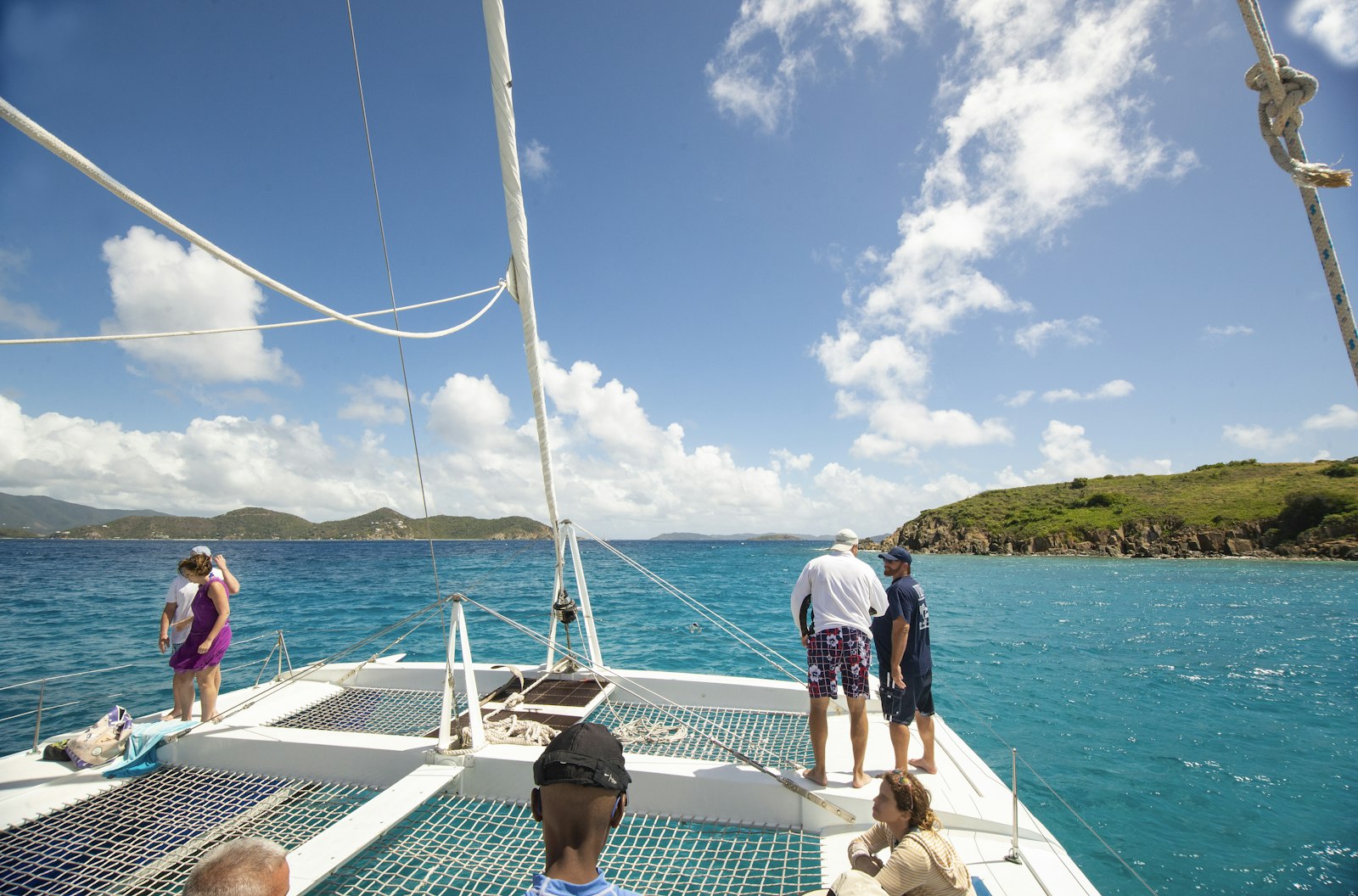 Guests standing on the bow net of a catamaran in turquoise water